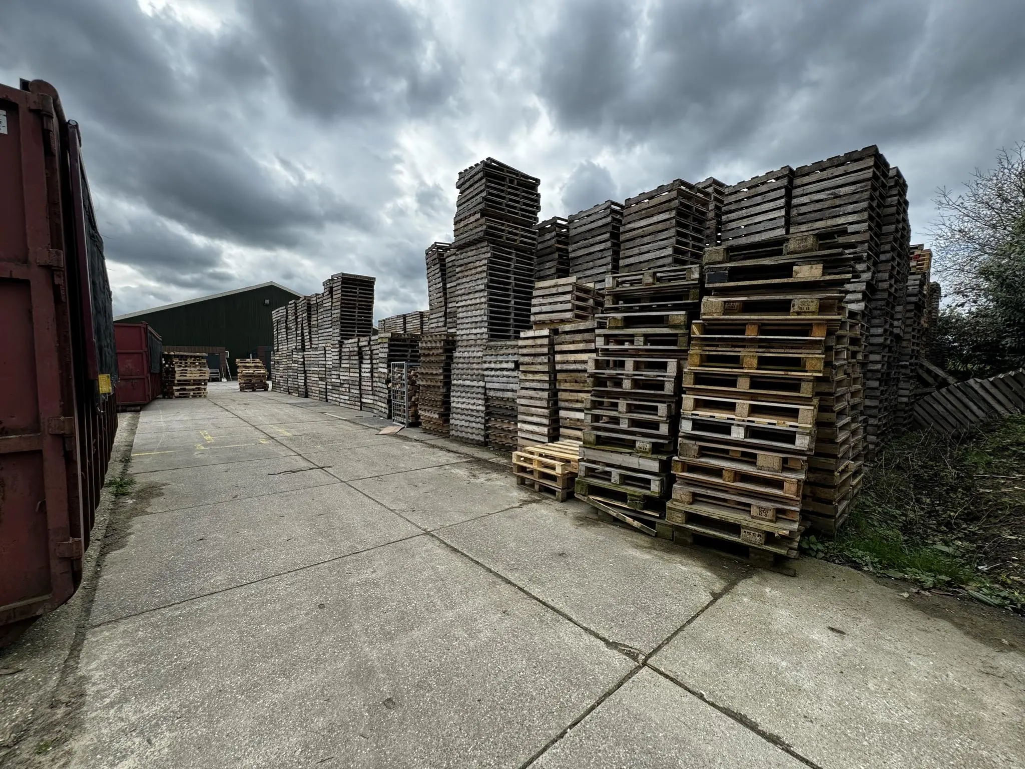 Hoge stapels houten pallets langs een betonnen weg op de Graaf van Lynden van Sandenburgweg.